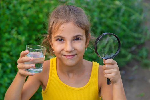 The child examines a glass of water with a magnifying glass. Selective focus. Kid.