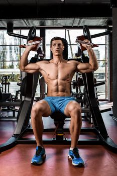 Tense muscles of hands under load. Man doing exercise for biceps in the gym. Work on tell muscles on the simulator. Photos for sporting magazines, posters and websites.