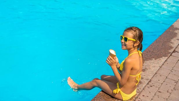 The child is eating ice cream near the pool. Selective focus. Kid.