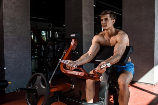 Tense muscles of hands under load. Man doing exercise for biceps in the gym. Work on tell muscles on the simulator. Photos for sporting magazines, posters and websites.