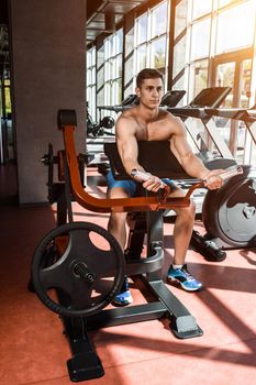 Tense muscles of hands under load. Man doing exercise for biceps in the gym. Work on tell muscles on the simulator. Photos for sporting magazines, posters and websites.