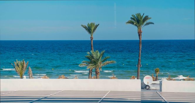 Beautiful mediterranean sea view from a hotel resort in Tunisia. Beach with palm trees, thatched sun umbrellas. Vacantion destionation in Africa. Tropical landscape.