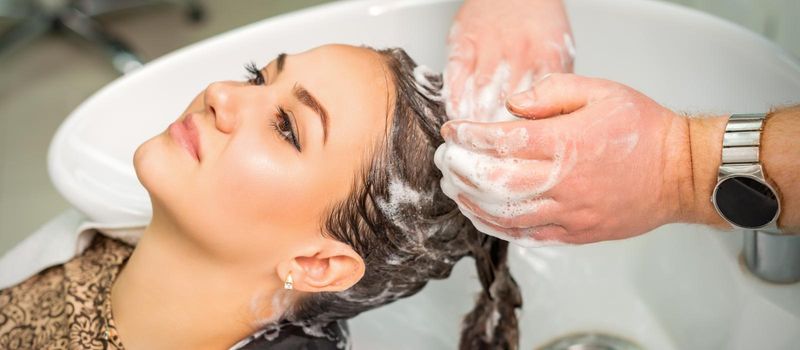 Beautiful young caucasian woman gets hair wash by male hands of hairdresser in hair salon