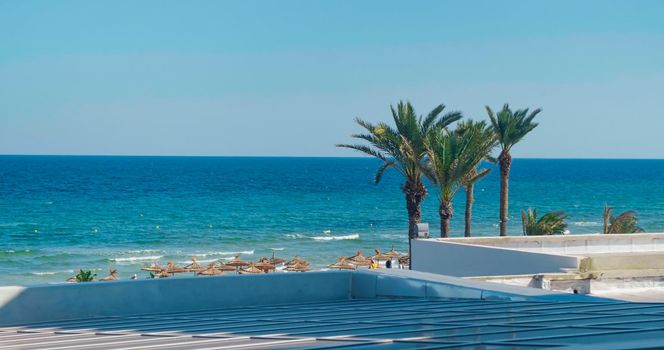 Beach resort on Mediterranean sea in Tunisia. Thatched sun umbrellas and palm trees on beach, luxury resort. Beautiful sea view from terrace.