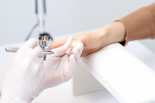 Young woman receiving manicure by airbrush in nail salon. Procedure for spraying paint on the nails