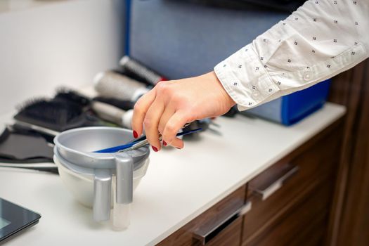 Hand of hairstylist prepares dye in bowl for coloring hair in hairdress salon