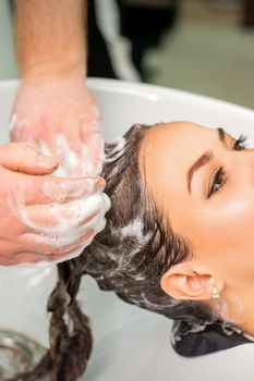 Beautiful young caucasian woman gets hair wash by male hands of hairdresser in hair salon