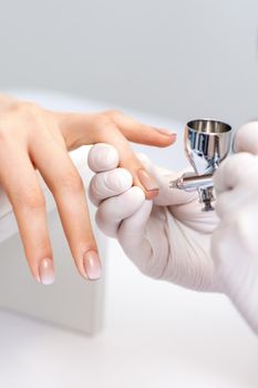 Young woman receiving manicure by airbrush in nail salon. Procedure for spraying paint on the nails
