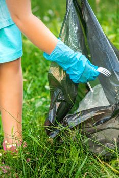 Child collects plastic trash from grass throwing garbage in garbage bag in the park