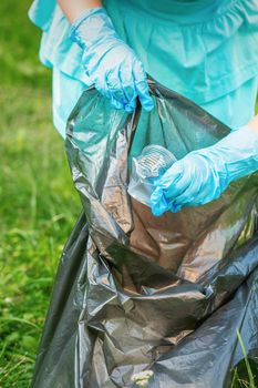 Child collects plastic trash from grass throwing garbage in garbage bag in the park