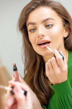 Beautiful young caucasian woman applying gloss to the lips looking in the mirror