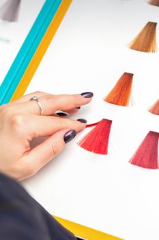 Customer's female hand choosing pink or red colour for hair colouring before hair dyeing in hair salon