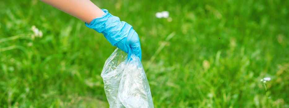 Hand of child cleans the park from plastic debris lying on the green grass