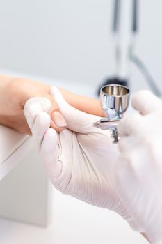 Young woman receiving manicure by airbrush in nail salon. Procedure for spraying paint on the nails