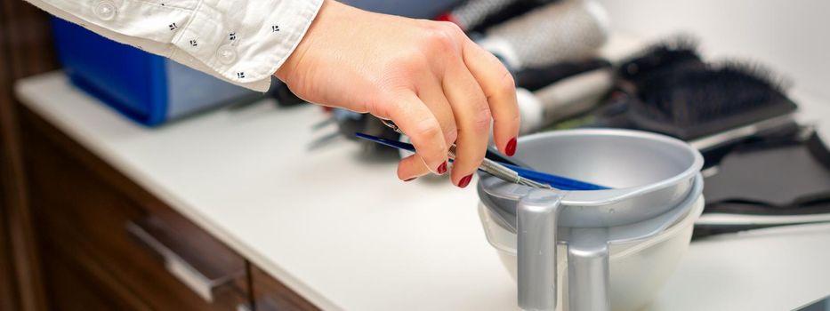 Hand of hairstylist prepares dye in bowl for coloring hair in hairdress salon