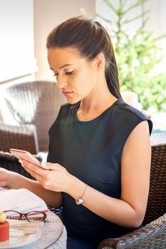 Young business woman makes notes in notebook from smartphone looking at it working at coffee break in cafe