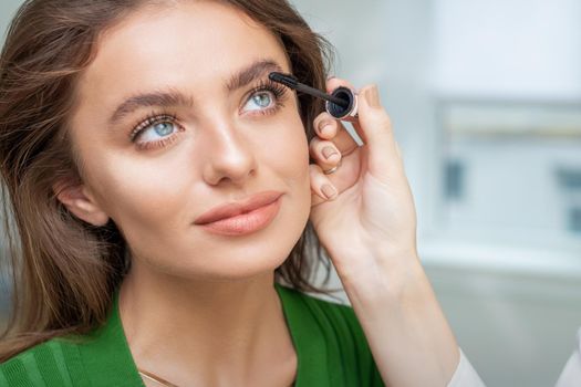 Professional makeup artist applying mascara on lashes of beautiful young caucasian woman in beauty salon