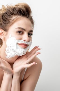 Beautiful young caucasian woman with shaving foam on her face posing on white background