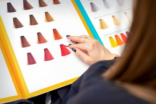 Customer's female hand choosing pink or red colour for hair colouring before hair dyeing in hair salon