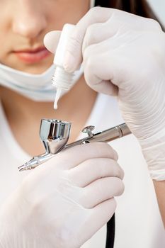 Manicure master adds white paint to airbrush before before the spraying procedure in nail salon