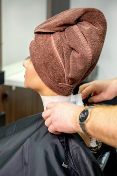 Hairdresser puts on black cape to female customer with towel on her head in hair salon