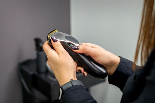 Hair clipper in hands of female professional hairdresser or barber in hair salon