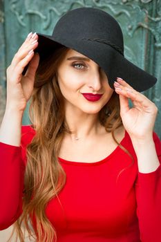 Portrait of beautiful fashionable caucasian young woman in red dress wearing black hat looking at camera