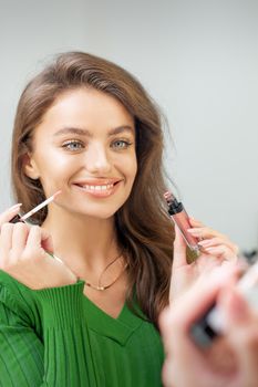 Beautiful young caucasian smiling woman applying gloss to the lips looking in the mirror