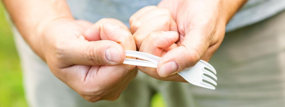 Male hand breaks plastic disposable fork in the park. The concept of environmental problems. Plastic free