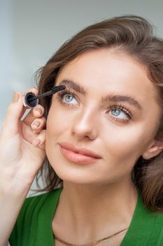 Professional makeup artist applying mascara on lashes of beautiful young caucasian woman in beauty salon