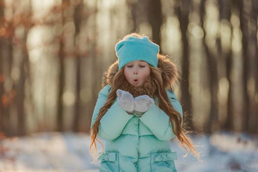 little girl blows on the snow that is on her mittens