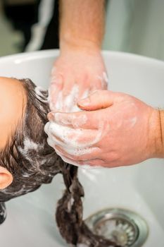 Beautiful young caucasian woman gets hair wash by male hands of hairdresser in hair salon