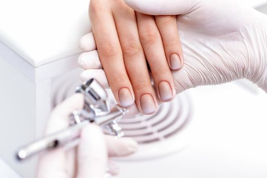 Young woman receiving manicure by airbrush in nail salon. Procedure for spraying paint on the nails