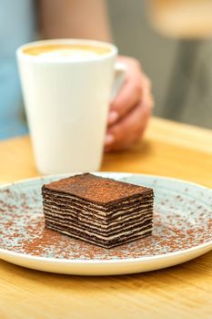 Piece of chocolate cake on plate with cup of coffee on the table in dessert cafe. Selective focus