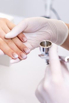 Young woman receiving manicure by airbrush in nail salon. Procedure for spraying paint on the nails