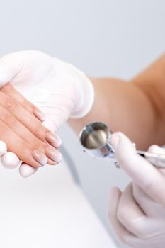 Young woman receiving manicure by airbrush in nail salon. Procedure for spraying paint on the nails