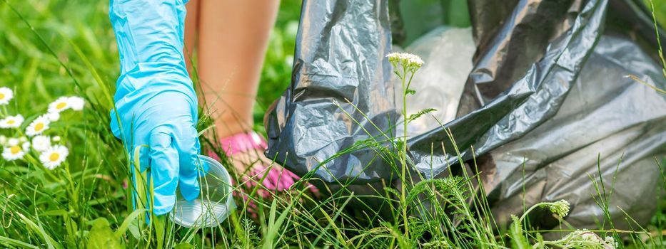 Child collects plastic trash from grass throwing garbage in garbage bag in the park