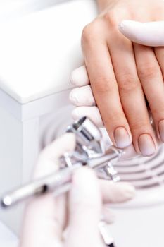Young woman receiving manicure by airbrush in nail salon. Procedure for spraying paint on the nails