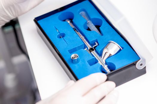 Close up shot of manicure master hand is taking out new clean airbrush tool for nails wearing gloves from the blue box