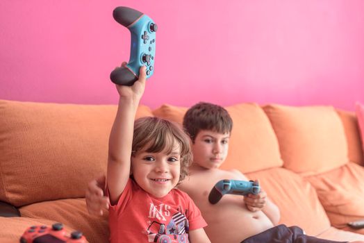 Computer game competition. Gaming concept. Excited children leaning on the sofa back playing video game with joysticks
