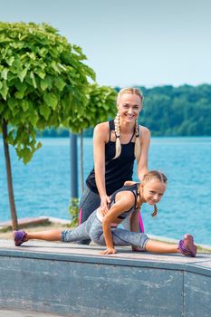 Mother and daughter doing gym exercises on the grass at the pier of the river