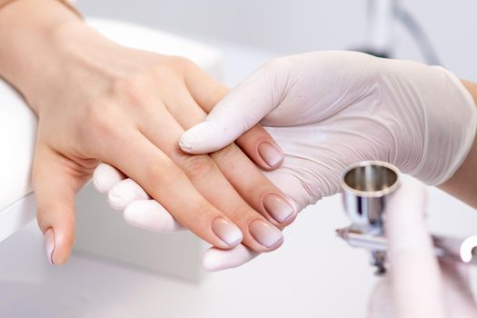Young woman receiving manicure by airbrush in nail salon. Procedure for spraying paint on the nails