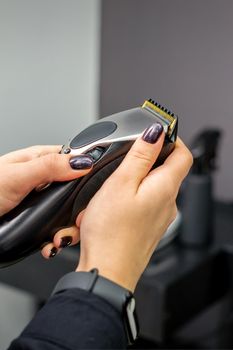 Hair clipper in hands of female professional hairdresser or barber in hair salon