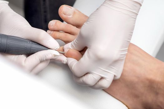 Process of professional pedicure. Pedicurist uses electric nail machine while doing pedicure on toes