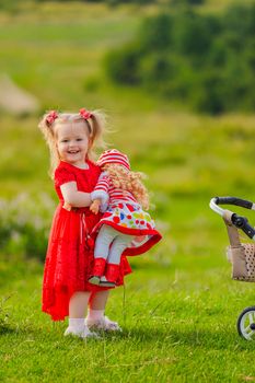 girl in a red dress and with a doll in her hands stands in nature