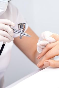 Young woman receiving manicure by airbrush in nail salon. Procedure for spraying paint on the nails