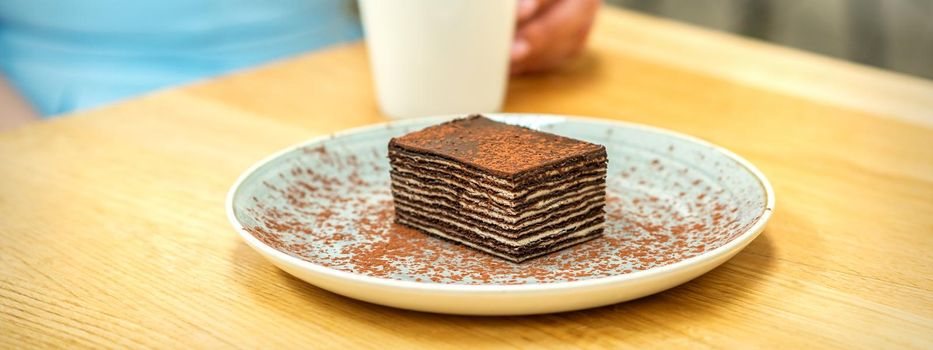 Piece of chocolate cake on plate with cup of coffee on the table in dessert cafe