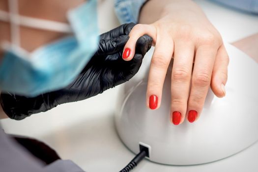 Young woman receives red nail polish by professional manicure master in nail salon