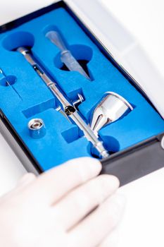 Close up shot of manicure master hand is taking out new clean airbrush tool for nails wearing gloves from the blue box