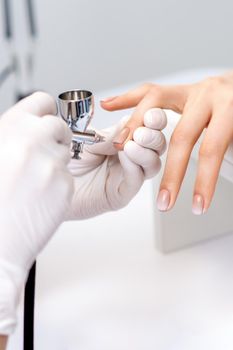 Young woman receiving manicure by airbrush in nail salon. Procedure for spraying paint on the nails